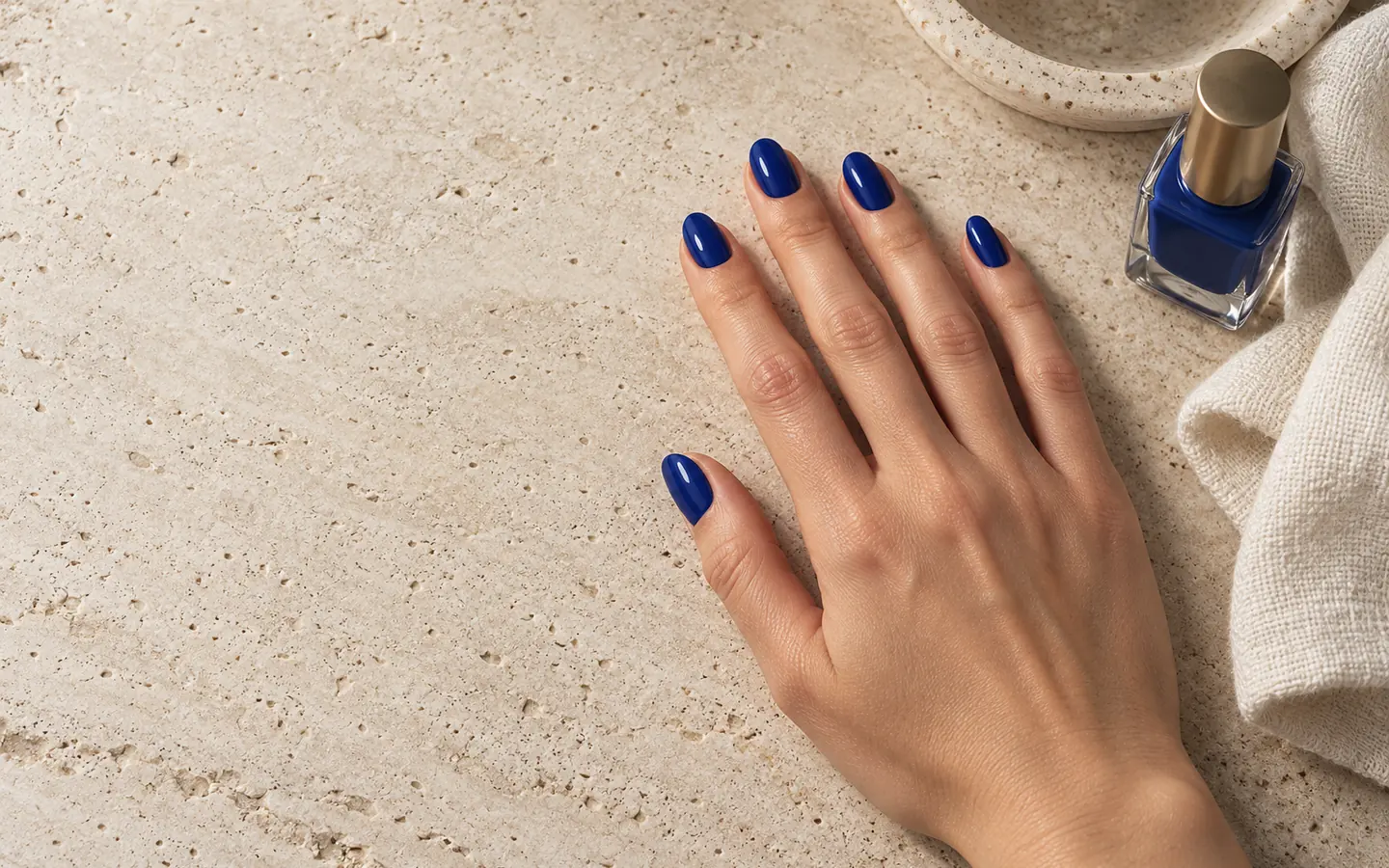 One relaxed hand on pale travertine, five short almond nails freshly painted in glossy ultramarine.